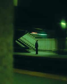 a man standing in the middle of a subway station at night with his back turned to the camera