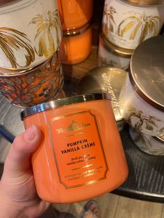 a hand holding an orange candle in front of some candles on a glass table top