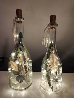 two glass bottles with lights in them sitting on a table