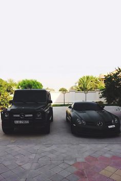 two black sports cars parked next to each other in front of a house with palm trees