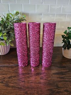 three pink vases sitting on top of a wooden table next to a potted plant