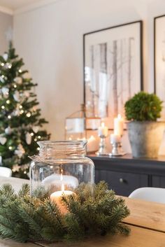 a candle in a glass jar sitting on top of a wooden table next to a christmas tree