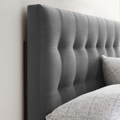 the headboard of a bed is made up with grey linens and silver pillows