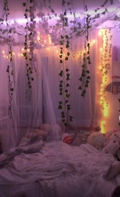 an unmade bed with white curtains and lights on the headboard is decorated with ivy vines