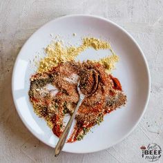 a white plate topped with spices and seasoning next to a spoon on top of a table