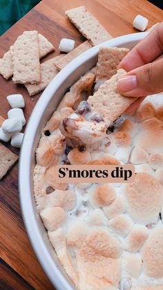 a person dipping marshmallows into a bowl of dip with graham crackers