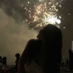 a woman standing in front of a firework display with her eyes closed and looking at the sky