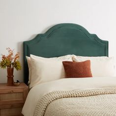 a green headboard on a bed with white linens and brown throw pillows in a bedroom