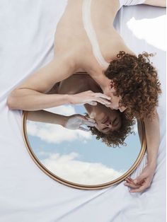 a naked woman laying in bed looking at herself in the mirror with her hands on her face