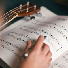 someone is writing on sheet music with a guitar in the backgroung behind them