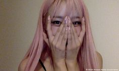 a woman with pink hair covering her face and hands over her eyes while standing in front of a wall