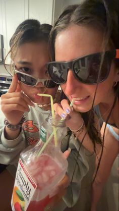 two girls wearing sunglasses and drinking drinks from a plastic bottle with straws in it