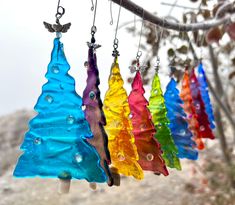 colorful glass christmas trees hanging from a tree branch in the wind with beads attached to them