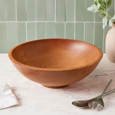 a wooden bowl sitting on top of a white counter next to a potted plant