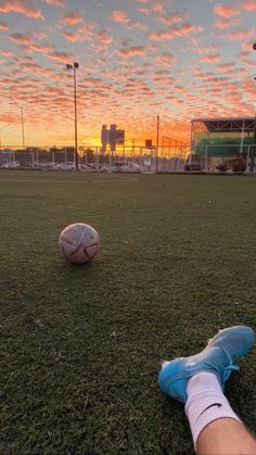 a person laying on the ground with a soccer ball in front of them and sunset behind them