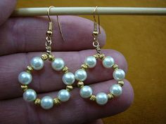 a pair of gold and white pearls are being held by a person's hand