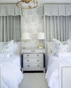 two twin beds in a bedroom with blue and white wallpaper, chandelier and curtains