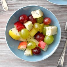 a blue bowl filled with fruit on top of a wooden table next to silverware