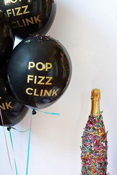 black balloons with pop fizz clink written on them next to a champagne bottle