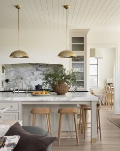 a kitchen with marble counter tops and gold pendant lights hanging from the ceiling, along with bar stools