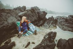 two people sitting on a beach with rocks and water in the background