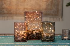 three glass vases filled with rocks and lights on top of a blue table cloth