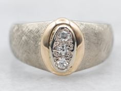 a gold and silver ring with two diamonds on it's center stone, sitting on a white surface