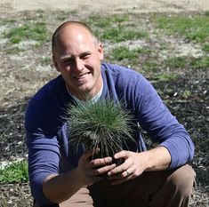 a man kneeling down next to a small plant in his hands and smiling at the camera