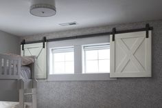 a bunk bed sitting next to two windows in a child's room with gray walls