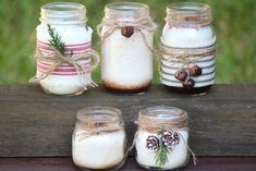 four mason jars with pine cones, cinnamons and other things in them sitting on a wooden table