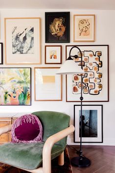 a green chair sitting in front of a wall with pictures on it and a lamp next to it