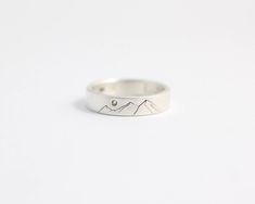 a silver ring with mountains on it and a diamond in the middle, against a white background