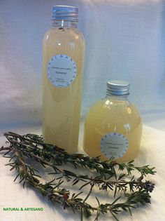 two bottles filled with liquid sitting on top of a white table cloth next to a sprig of rosemary