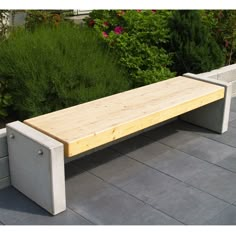 a wooden bench sitting on top of a cement block next to bushes and flowers in the background