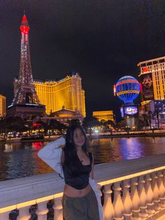 a woman standing next to a railing in front of the eiffel tower at night