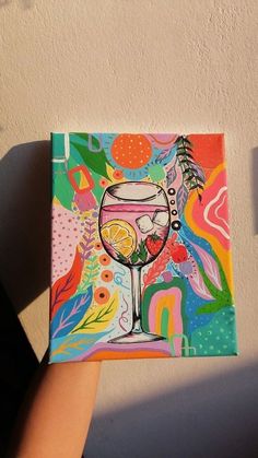 a hand holding up a colorful painting with a wine glass on it