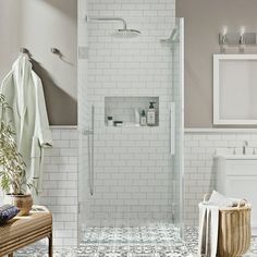 a white tiled bathroom with a walk in shower next to a wicker chair and towel rack