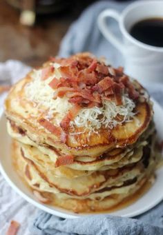 a stack of pancakes topped with bacon and grated cheese on a plate next to a cup of coffee