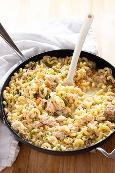 a skillet filled with pasta and meat on top of a wooden table next to a white towel