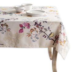 the table cloth has birds on it and is next to two plates with cups on them