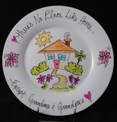 a white plate with a house and flowers painted on the front, saying there is no place like home