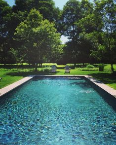 an empty swimming pool in the middle of a lush green park with benches and trees