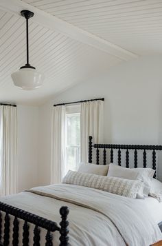 a bed with white sheets and pillows in a bedroom next to two windows that have curtains on them