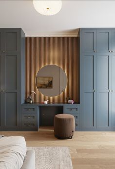 a bedroom with blue cupboards and a round mirror on the wall, along with a stool