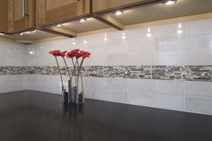 some red flowers are sitting in a vase on the kitchen counter top with white tiles