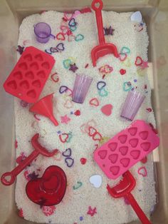 a tray filled with sand and plastic utensils next to heart shaped ice cream molds