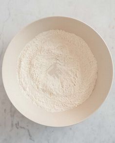 a white bowl filled with flour on top of a marble counter