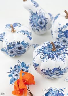 blue and white painted pumpkins with orange flowers in the middle on a white surface