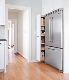 a stainless steel refrigerator in a kitchen with white cabinets and wood flooring on the side