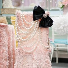 two pink dresses with pearls and a black bow on the back are sitting next to each other